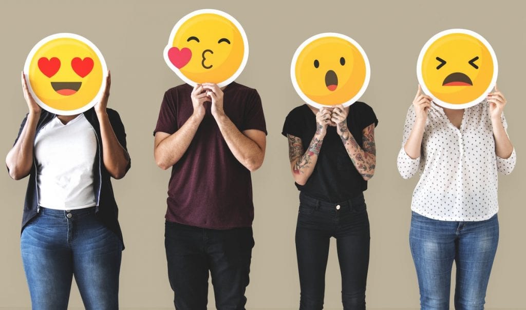 Four people holding emojis in front of their faces
