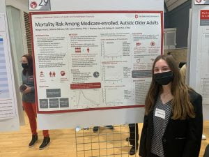Photo of Morgan Krantz facing the camera, standing next to her research poster titled "Mortality Risk Among Medicare-Enrolled Autistic Adults" 