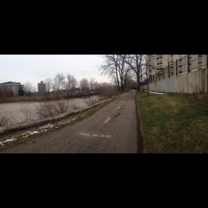 The trail is paved and is wide enough with lines so people can walk, run, and bike. The building to the right and the buildings across the river remind you that you are in an urban setting. The river and the trees farther down along the trail are trying to get the people away from the city.