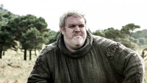 Hodor grimaces while looking to the side. He has white hair and is wearing a large gray tunic.