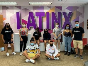 Group of masked students pose in front of Latinx wall mural