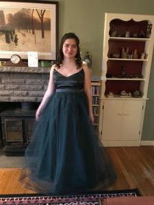A girl is standing in a dark green tulle dress in front of a fireplace.
