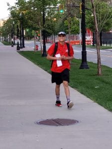 Young man in red Ohio State shirt walking down the sidewalk with a big smile on his face. 