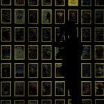 Wall of National Geographic Magazines Covers with a photographer in front. dark picture and the yellow edging on the covers glow